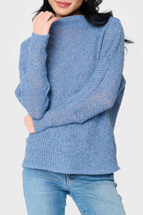 A woman wearing an off shoulder, slouchy sweater in a natural color, paired with blue jeans.