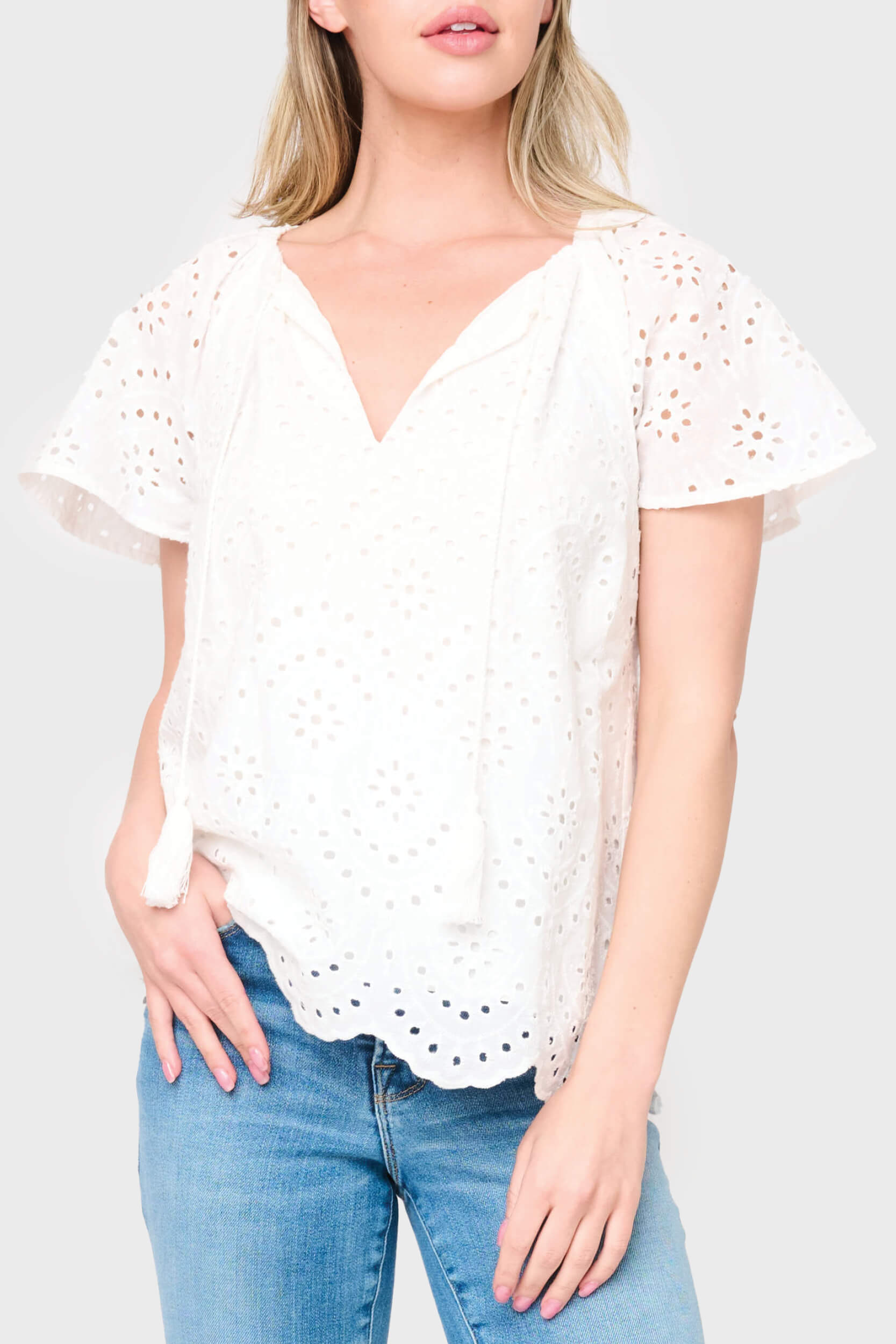 Woman modeling Flutter Sleeve Scallop Top in White eyelet styled with denim