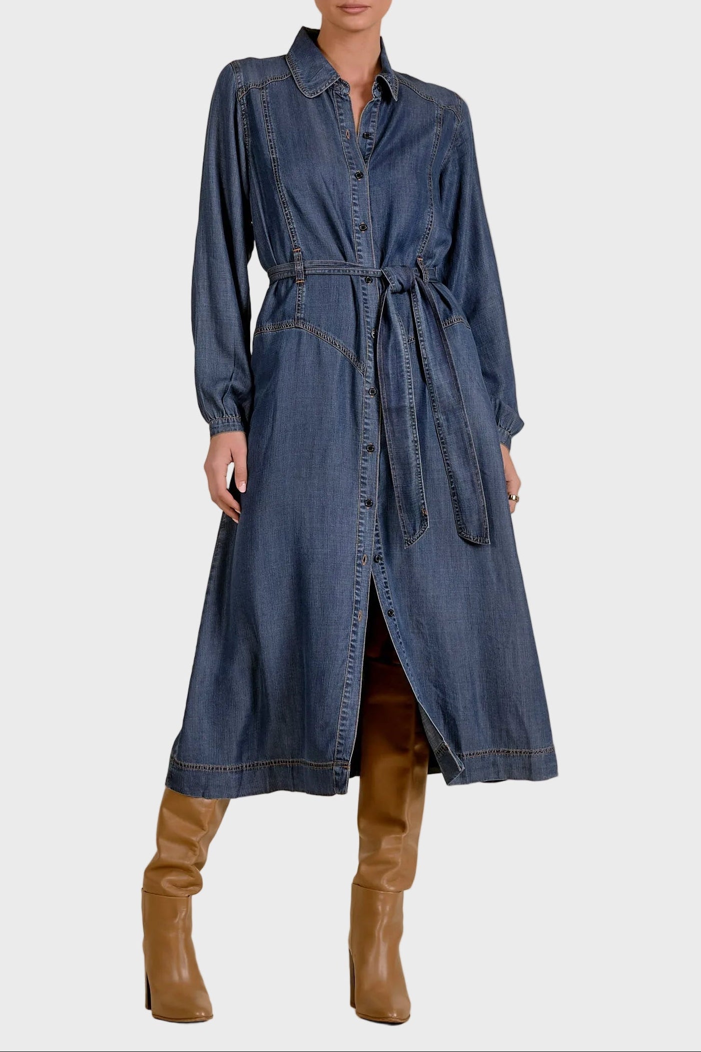 Woman wearing a long denim dress with brown boots on a beige background