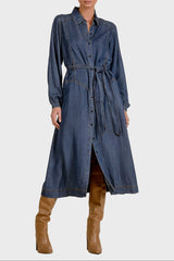 Woman wearing a long denim dress with brown boots on a beige background