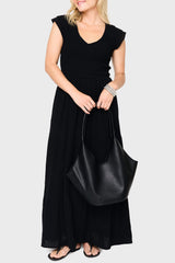 Woman modeling Flutter Sleeve Smocked V-Neck Tiered Maxi Dress in Black, styled with handbag for dinner