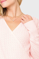 Close-up of a person wearing a pink sweater and gold necklace with a small pendant on a light gray background