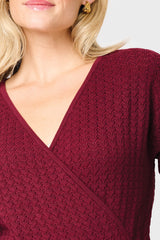 Close-up of a person wearing a burgundy knitted sweater on a light gray background