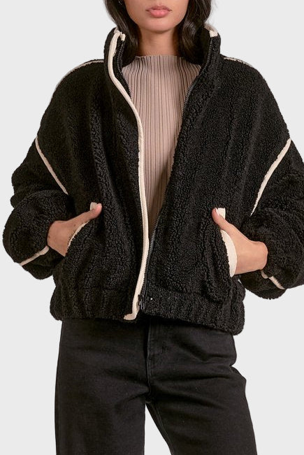 Woman wearing a black sherpa jacket with white trim on a plain background