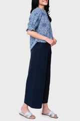 Side view Women modeling Dianthus Henley Puff Sleeve Blouse in Bandana Blue print style with linen pants and sandals