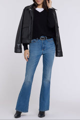 A woman modeling a black faux-leather moto jacket, black sweater, blue flare jeans, and black boots against a light gray studio background.