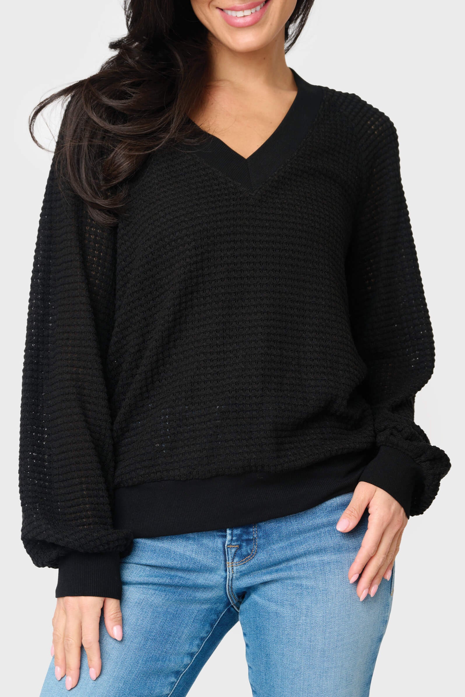 A woman wearing a black v-neck, open weave sweater paired with blue jeans.