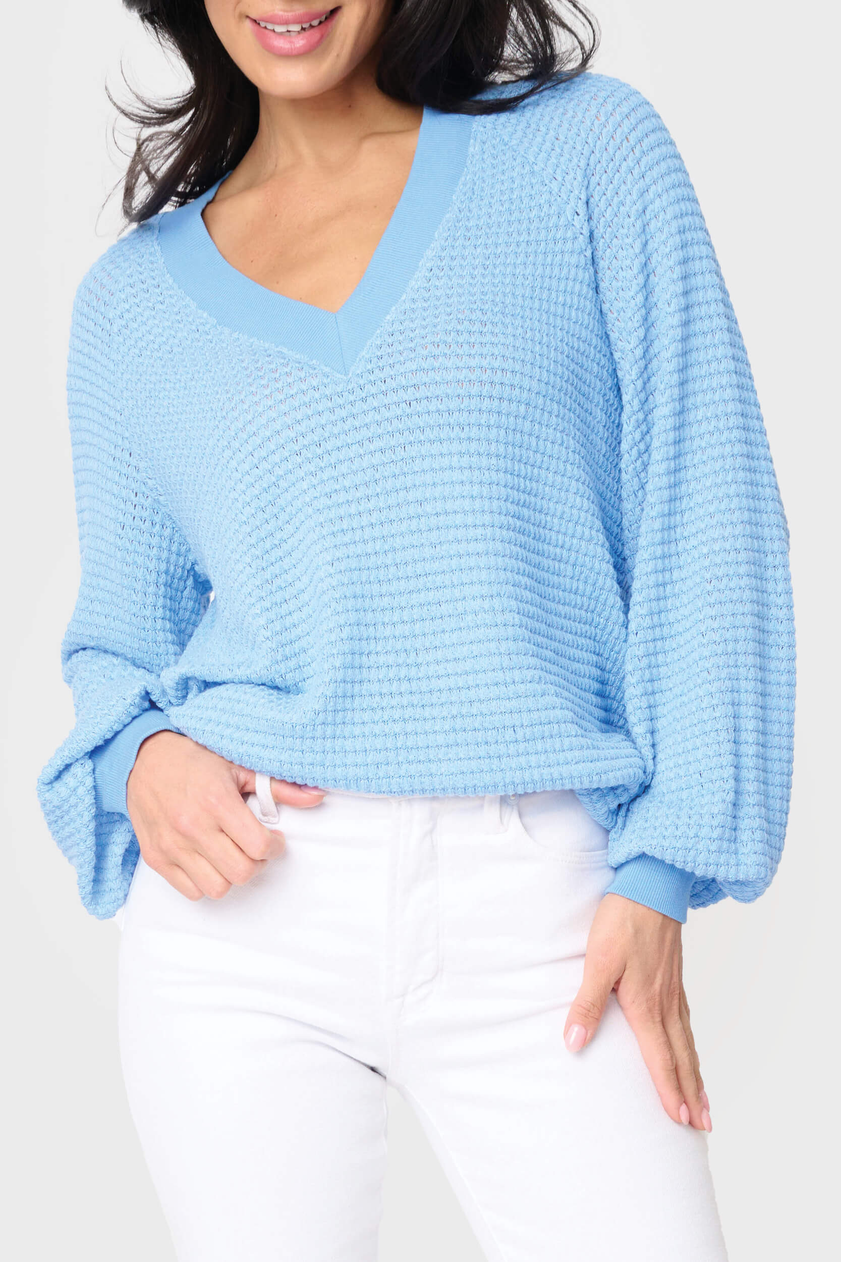 A woman wearing a blue v-neck, open weave sweater paired with white jeans.