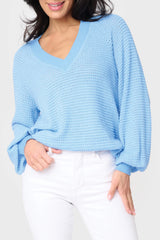 A woman wearing a blue v-neck, open weave sweater paired with white jeans.