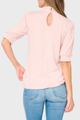 Person wearing a light pink blouse with a cutout back design and blue jeans on a white background