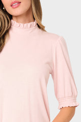 Close-up of a person wearing a light pink blouse with ruffled collar and cuffs on a white background