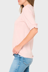 Person wearing a light pink blouse with rolled-up sleeves and blue jeans on a white background