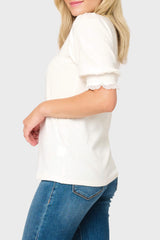 Woman wearing a white blouse with ruffled sleeves and blue jeans on a plain background