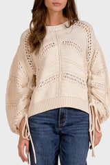 Beige knitted sweater with lace details worn by a person on a beige background
