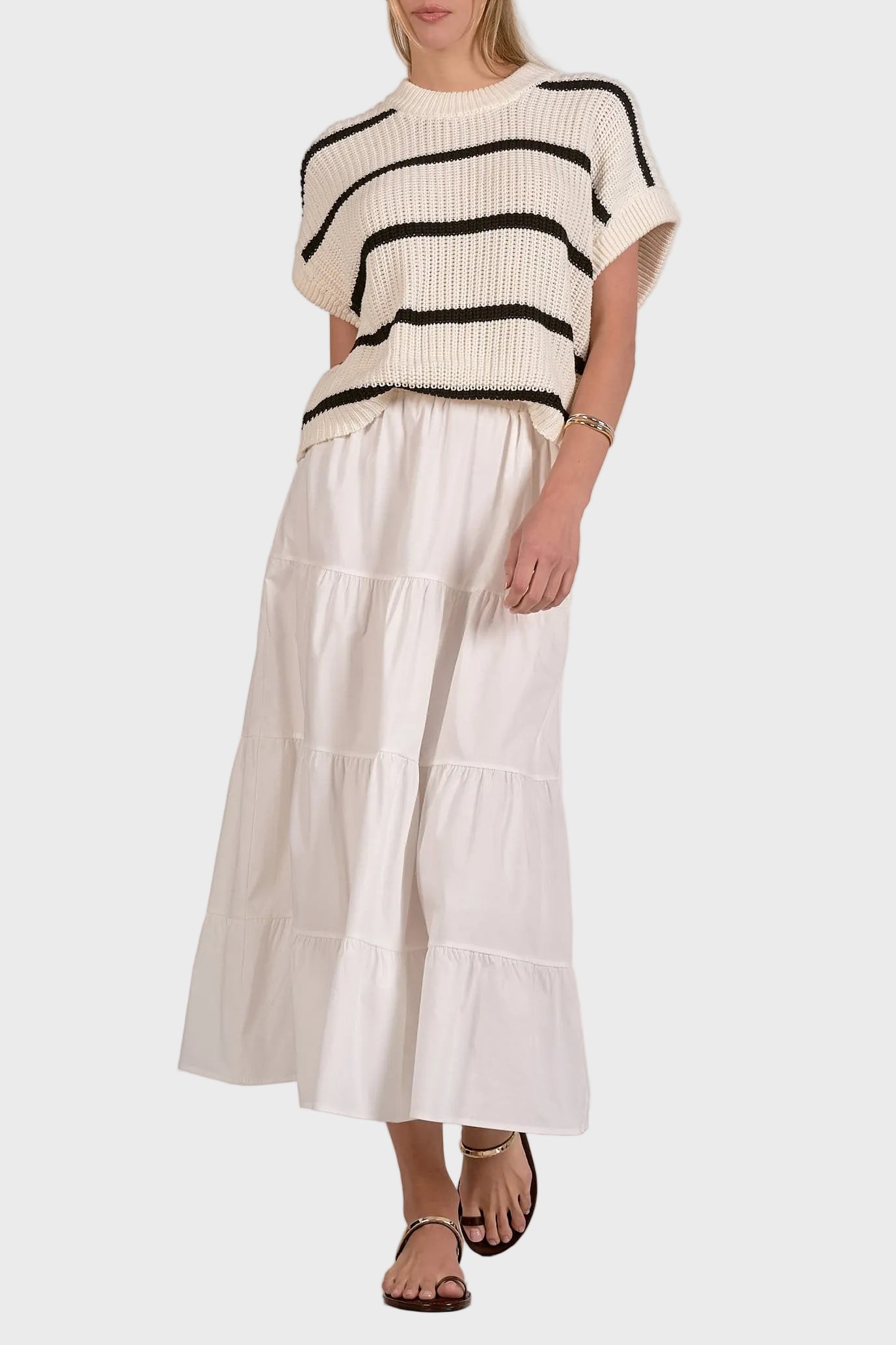 Woman wearing a black and white striped sweater with a white tiered skirt on a plain background