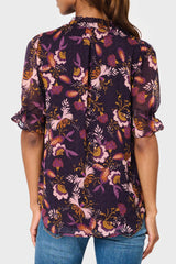 Back of Model wearing Dianthus Henley Puff Sleeve Chiffon Blouse in Purple floral print styled for work