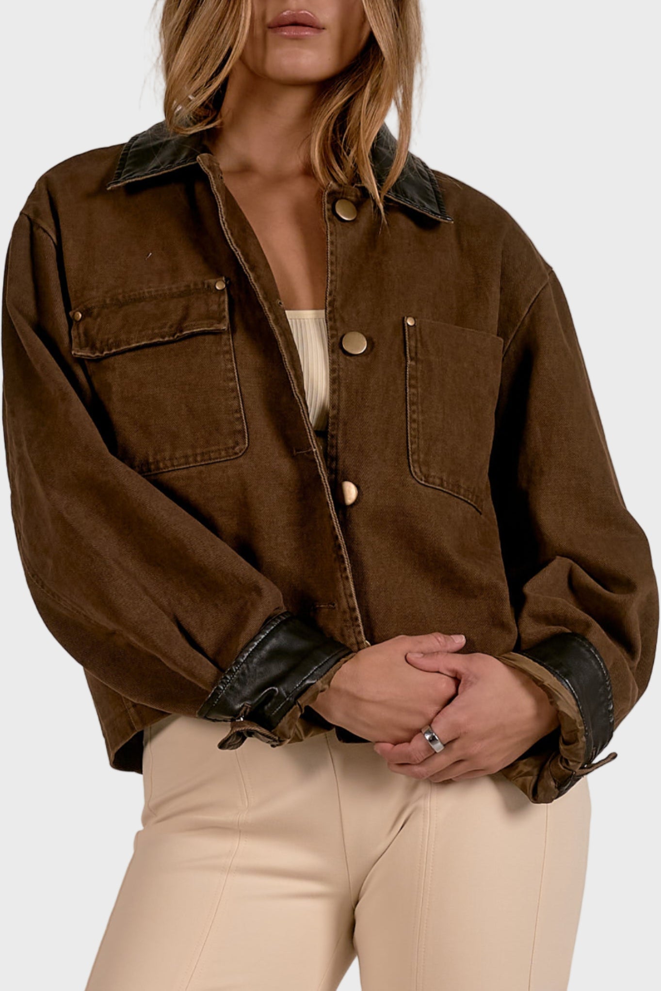 Woman wearing a brown jacket with black collar and cuffs on a plain background
