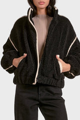 Woman wearing a black sherpa jacket with white trim on a plain background