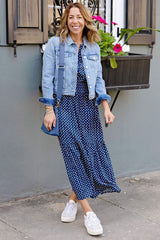 @themotherchic Woman modeling Lindsey Utility Maxi Dress in Navy Daisy print styled with sneakers and jacket