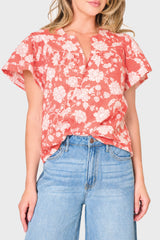 Woman modeling Flutter Sleeve Blouse With Open Yoke in coral orange floral print styled with denim for everyday
