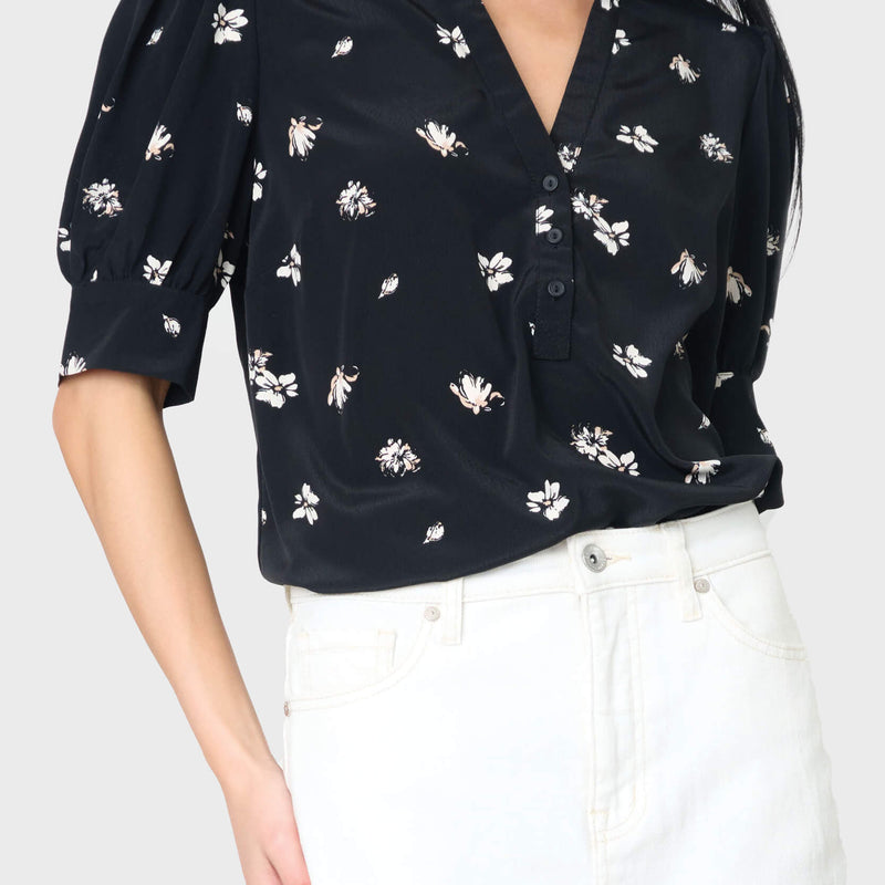 A black woven henley blouse with puff sleeves, floral print, paired with white trousers.