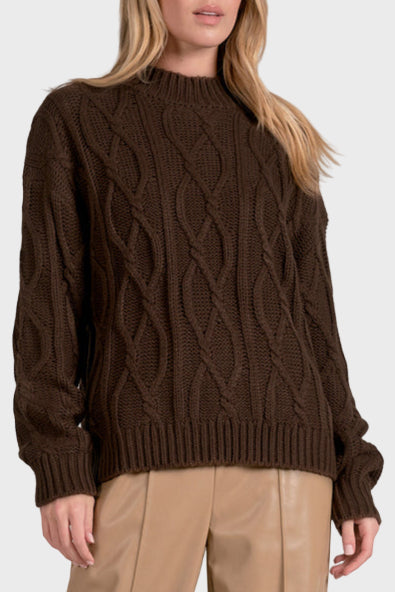 Woman wearing a brown cable knit sweater and beige pants on a white background