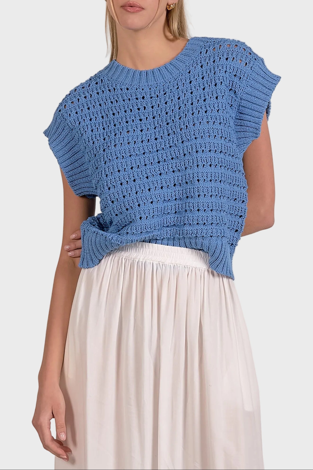 Woman wearing a blue knitted top and white skirt on a plain background