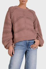 Woman wearing a brown knitted sweater and blue jeans against a beige background